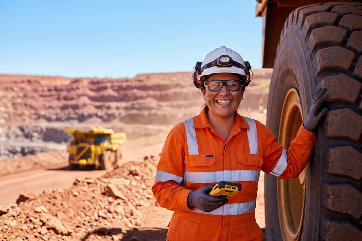 A smiling mine maintenance supervisor wearing Visor glasses beside a haul truck tyre in an open pit